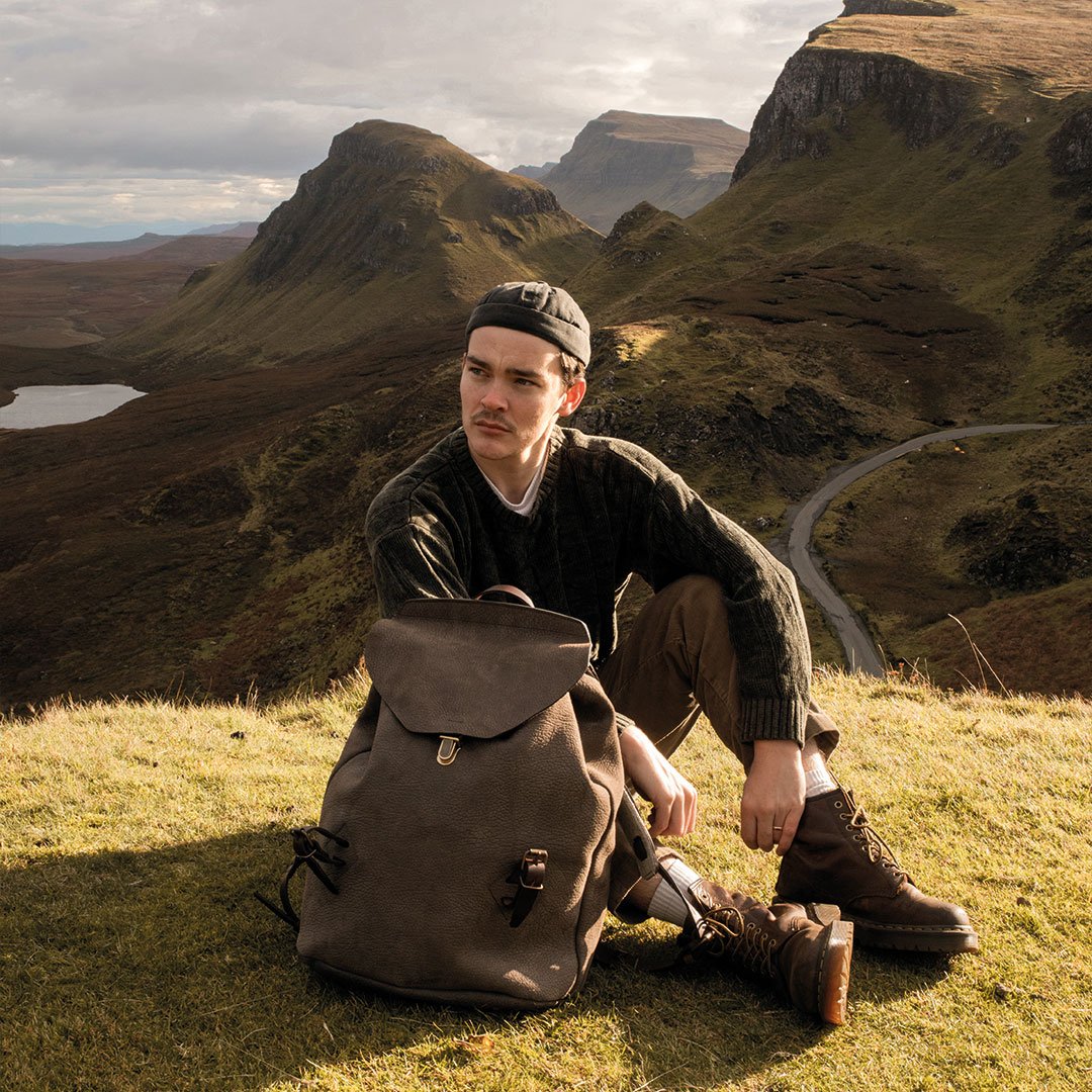 Un homme assis dans la nature a coté de son sac a dos en cuir