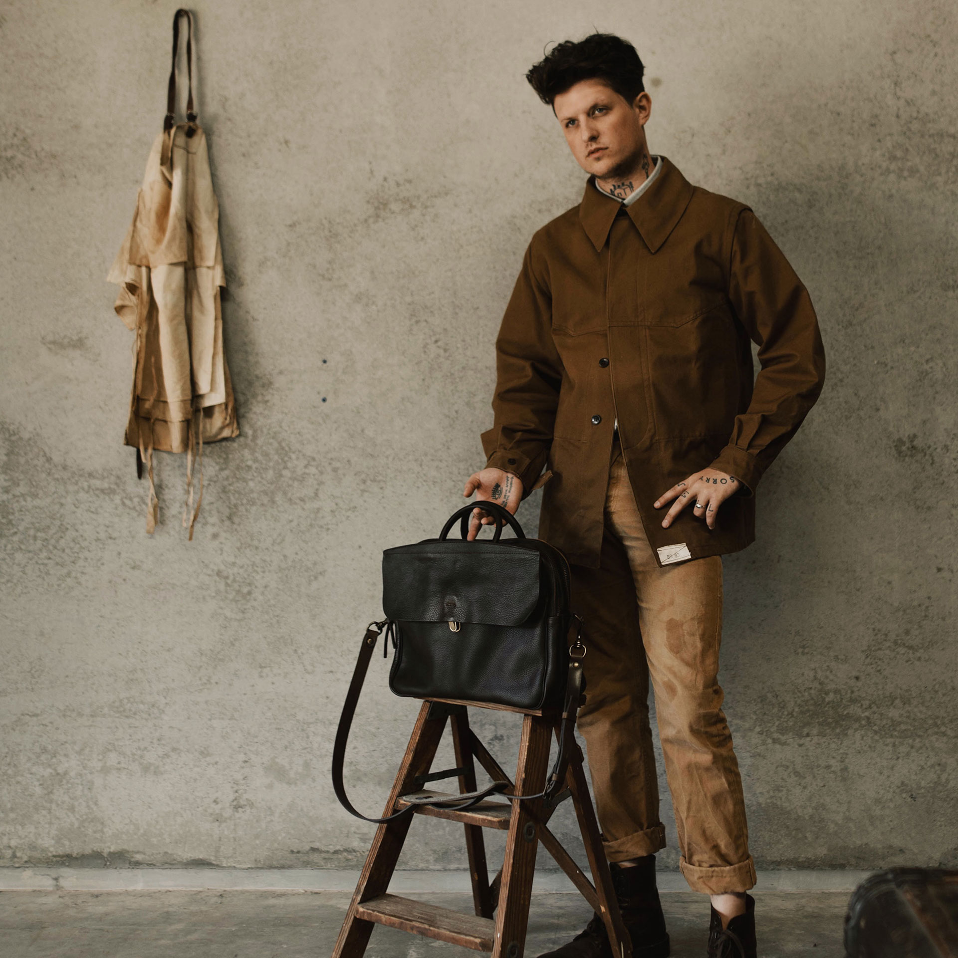 Un homme au style workwear se porte a coté de son sac en cuir