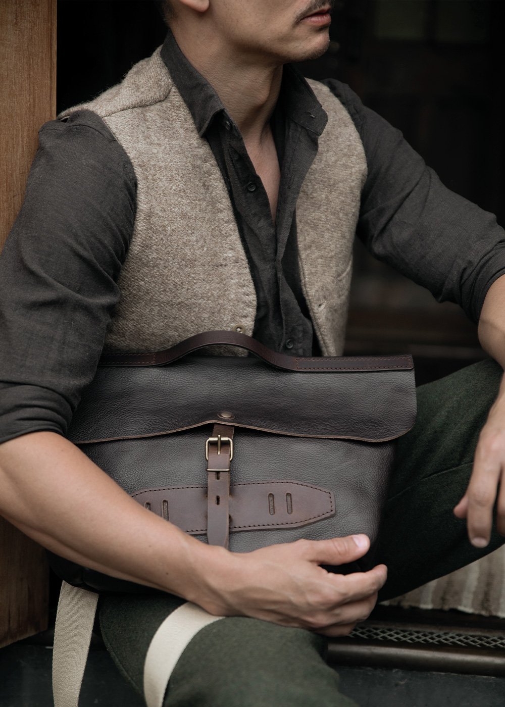 Un homme en tenue workwear porte a la main son sac besace en cuir 